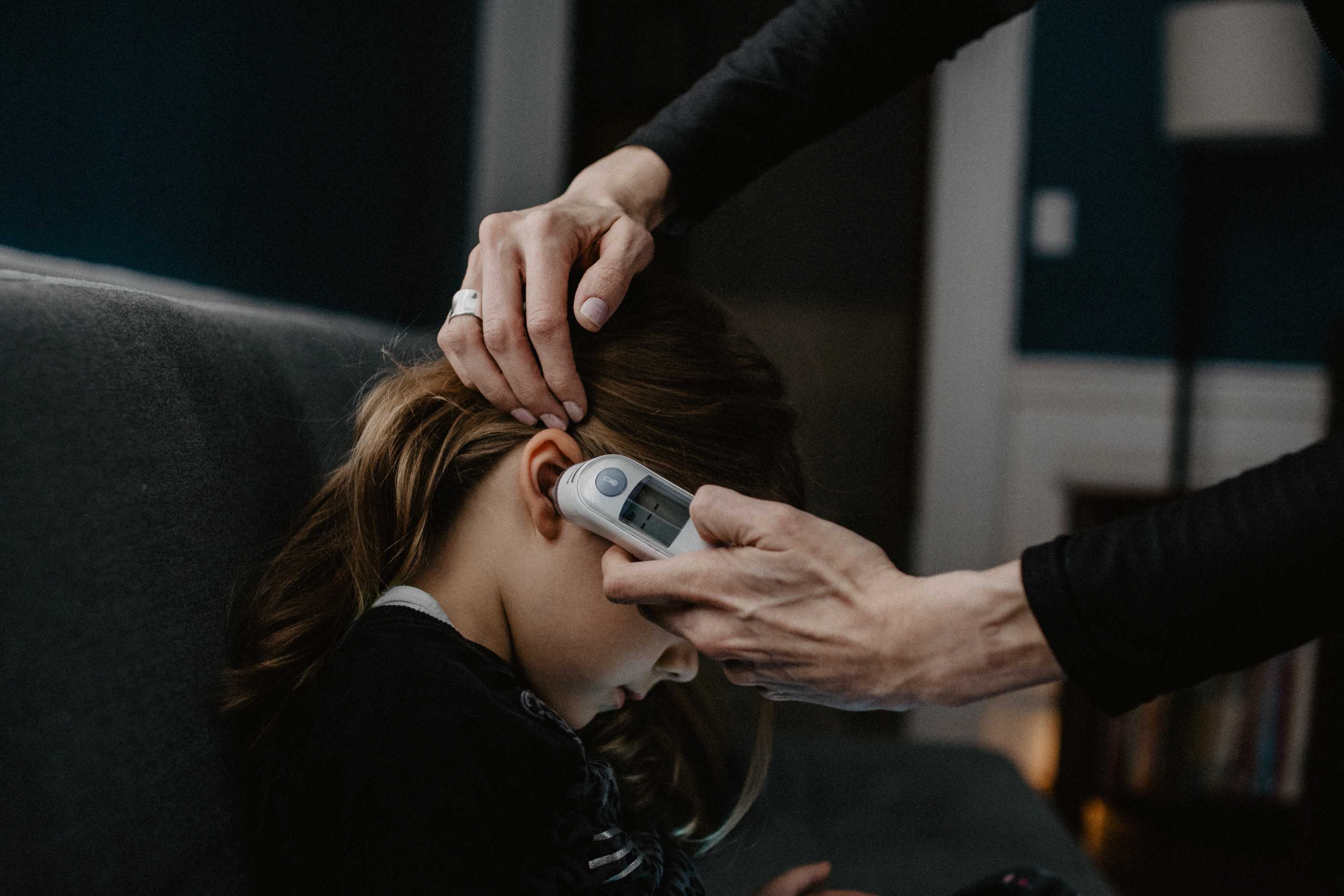 Close up of an adult's hand holding an in-ear thermometer to a child's ear.